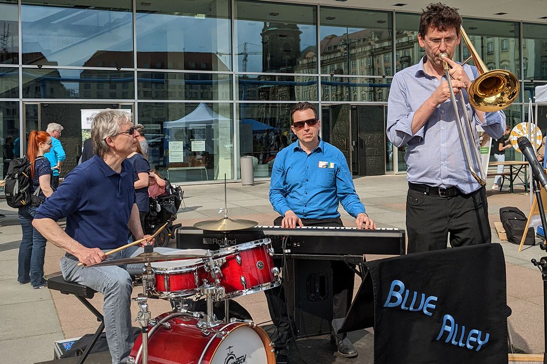 Die Jazzband Blue Alley spielt auf der Bühne: Sie besteht aus einem Pianisten, einem Trompeter und einem Schlagzeuger.