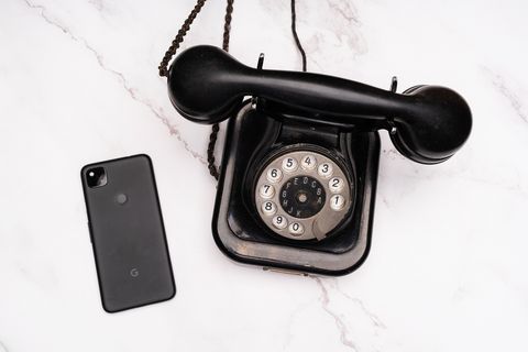 Ein schwarzes Smartphone (links) neben einem klassischen, schwarzen Wahlscheibentelefon (rechts)