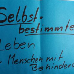 Blaues Protestplakat mit schwarzer Aufschrift: Selbstbestimmtes Leben für Menschen mit Behinderung