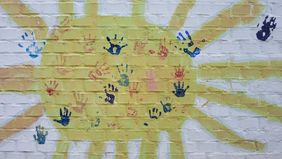 gemalte Sonne mit bunten Handabdrücken in der Mitte