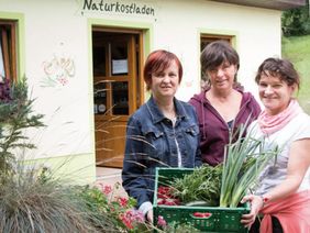 Drei Frauen stehen vor dem Hofladen und halten einen Korb mit Gemüse in die Kamera