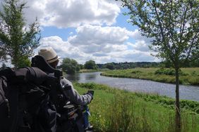 Rollstuhlnutzerin blickt auf Fluss, Perspektive aus ihrer Höhe, allerdings von hinten