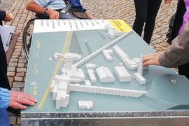 Ein Tastmodell des Bergbaumuseums. Es stehen Menschen um das Modell herum und drei Hände betasten es vorsichtig