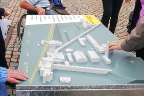 Ein Tastmodell des Bergbaumuseums. Es stehen Menschen um das Modell herum und drei Hände betasten es vorsichtig