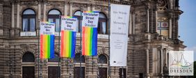 An der Fassade der Semperoper in Dresden hängen die Flaggen der LGBTQ-Bewegung in den Farben rot, pink, gelb, grün, blau. Darüber und daneben ist mehrfach der Schriftzug "Christopher Street Day Dresden" zu lesen.