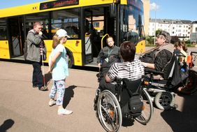 Rollstuhlnutzer stehen vor dem Bus und hören einem Mann im Rollstuhl zu