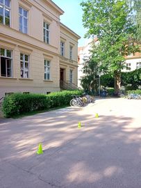 Der Schulhof der Heise Schule in Görlitz. Auf ndem Schulhof ist ein Rollstuhlparcour mit gelben Kegeln abgesteckt. Vor dem Schulgebäude steht eine Hecke, vor der 4 leere Rollstühle stehen