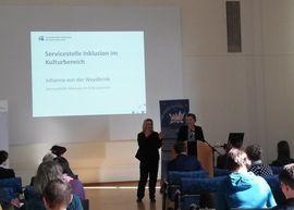 Frau spricht vor Publikum, dazu übersetzt eine Gebärdendolmetscherin
