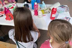 Zwei kleine Mädchen sitzen an unserem Bastelstand und malen. Auf dem Tisch stehen viele Farben und gebastelte Werke.
