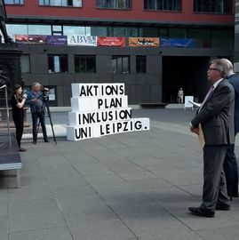 Stephan Pöhler als Zuhörer und Blick auf Kartonstapel mit der Aufschrift: Aktionstag Inklusion an der Uni Leipzig