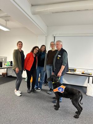 Mitarbeiterinnen des Jobcenters, Kerstin Helm und zwei Mitarbeiter des BSVS stehen nebeneinander und lächeln in die Kamera. Vor ihnen steht ein brauner Blindenhund.