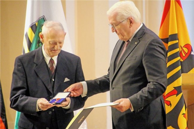Bundespräsident Frank-Walter Steinmeier überreicht Immo Stamm das Bundesverdienstkreuz. Beide sind in Anzüge gekleidet. Îmmo Stamm hält die geöffnete Schachtel mit dem Bundesverdienstkreuz in den Händen. 