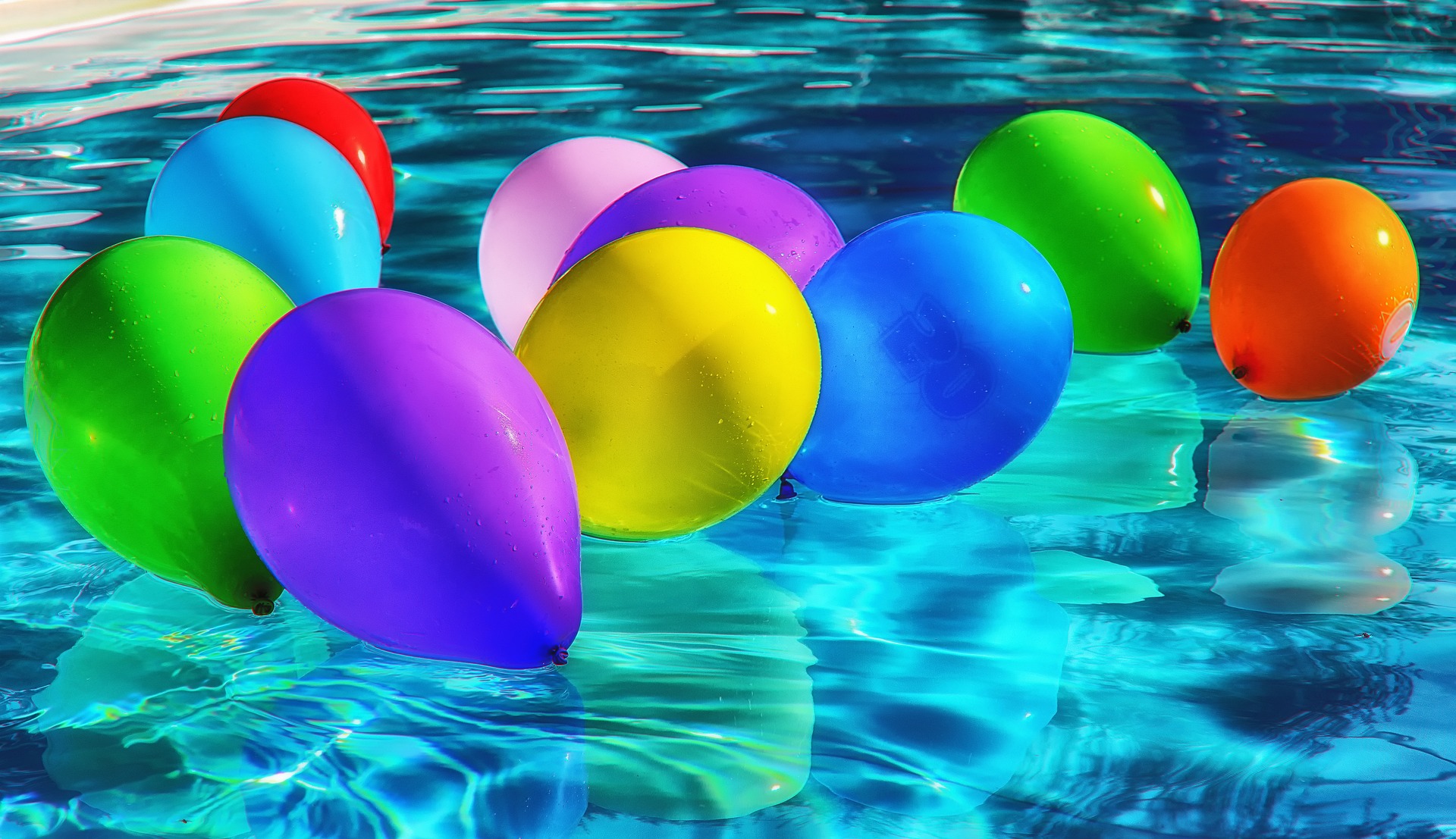 verschiedenfarbige Ballons die in einem Schwimmbecken auf dem Wasser treiben